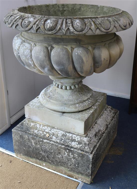 A pair of reconstituted stone garden urns, of campana shape, raised on stepped plinths